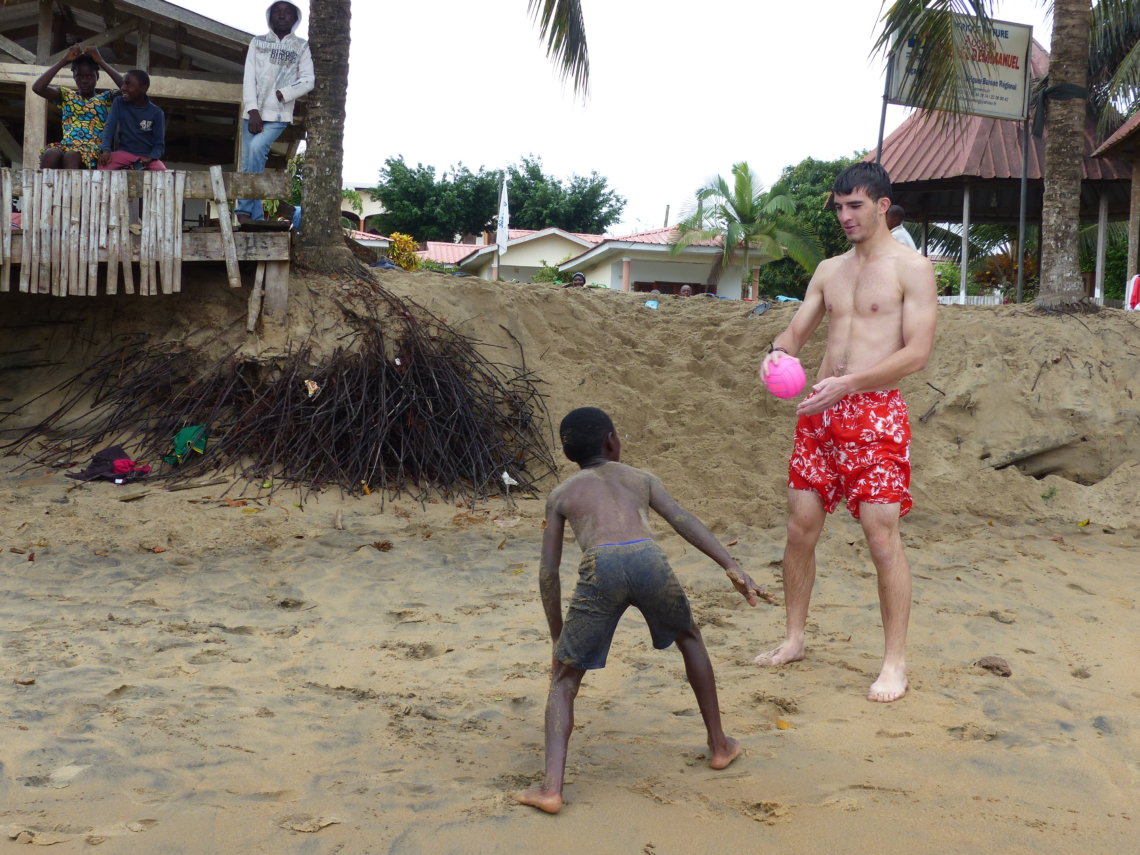 un enfant et un jeune homme joue au foot à la plage